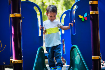 3 year old boy looks unsure about going down a slide as he looks down at the edge of the playground slide.