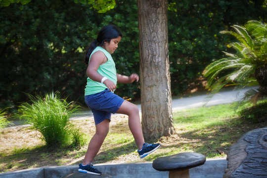Pre teen girl jumping from one step to another at a kids playground, doing physical activity that develops her sence of balance.