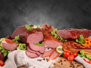 Different types of smoked meat pieces and slicing on canvas napkins and a wooden Board with herbs and vegetables. On black backgraund.