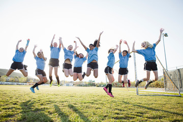 Happy girls in soccer uniforms with arms raised jumping on grassy field against sky © Cavan for Adobe