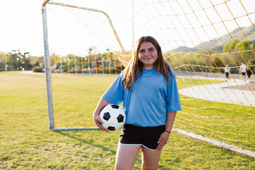 Portrait of smiling girl holding soccer ball standing on grassy field against net © Cavan for Adobe