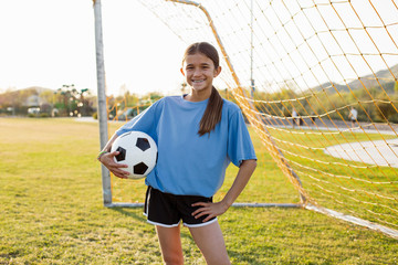 Portrait of cheerful girl holding soccer ball while standing on grassy field against clear sky © Cavan for Adobe
