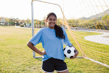 Portrait of smiling soccer player with ball standing on grassy field against clear sky © Cavan for Adobe