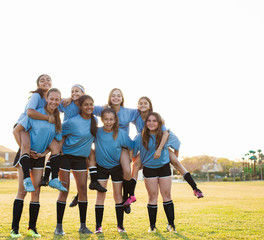 Low angle portrait of girls piggybacking friends while standing on soccer field against clear sky during sunset © Cavan for Adobe