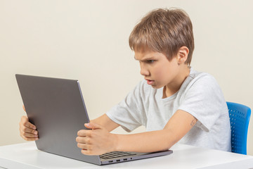 Angry sad boy with laptop computer sitting at the table
