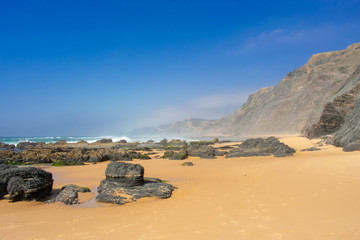 Fototapeta na wymiar Rock formations and cliffs on beach, high waves on water of Atlantic Ocean. West coast of Algarve Portugal