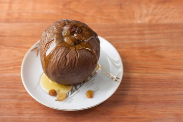 Baked apple stuffed with raisins and walnuts and honey poured on a white plate on a wooden background.