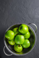 Fresh juicy green apple in stainless steel colander on Dark grey black slate background