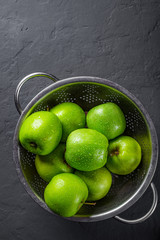 Fresh juicy green apple in stainless steel colander on Dark grey black slate background