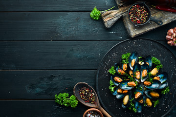 Boiled mussels with parsley and spices on a black plate. Top view. Free space for your text.