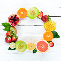Fruits on a white wooden background. Mango, melon, pomegranate, strawberry, banana. Top view. Free space for your text.