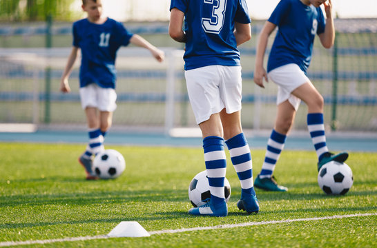 Legs of european football boys kicking balls on field. Group of young football players on soccer training. Football practice training background