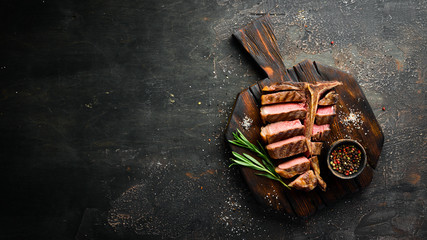 Beef T-Bone steak on a black table. Top view. Free space for text.