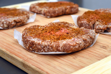 Seasoned raw hamburger patties on wooden cutting board