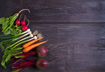 Carrots, beet, radishes, onions, garlic, spinach - root vegetables on a black wooden background. Summer farm vegetables. Food background, layout, room for text