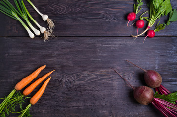 Carrots, beet, radishes, onions, garlic, spinach - root vegetables on a black wooden background. Summer farm vegetables. Food background, layout, room for text