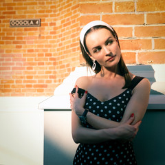 A girl in a polka dot dress by the brick wall. Retro style