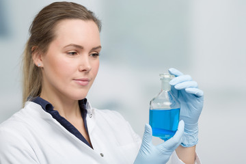 young female chemist with a liquid sample in front of laboratory