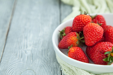 Juicy fresh strawberries in a white plate on a grey wooden background, selective focus