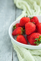 Juicy fresh strawberries in a white plate on a grey wooden background, selective focus
