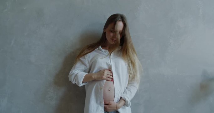 Happy caucasian pregnant women with big belly standing and rubbing her belly. 60 fps