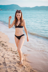 Fototapeta na wymiar Beautiful woman in black bikini is walking from sea, summer concept