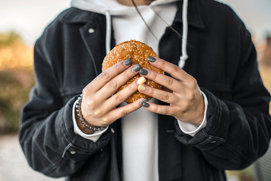 Hands of young woman with painted nails holding a hamburger, close-up
