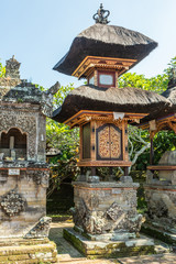 Ubud, Bali, Indonesia - February 26, 2019: Batuan Temple. Closeup of small shrine among others. Golden-brown tabernacle=like box and double reed roof under blue sky. Some green foliage.