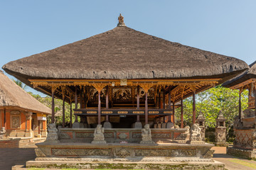 Ubud, Bali, Indonesia - February 26, 2019: Batuan Temple. Large open shrine with reed roof set on green lawn under blue sky. White stone statues and gold decorations.