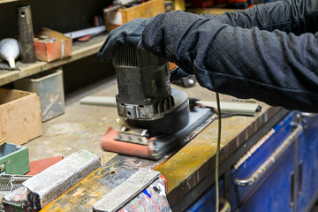 Eine Frau schleift mit einer Schleifmaschine den Rost von einem St&uuml;ck Eisen