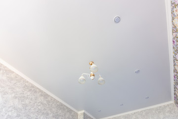 Stretch ceiling in a room with a chandelier and spotlights, with natural light