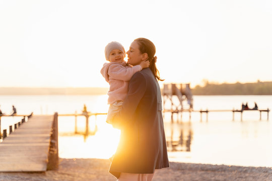 Germany, Bavaria, Herrsching, mother carrying daughter at the lakeshore at sunset