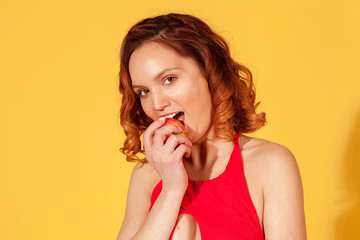 girl on yellow background in red swimsuit taking a bite of the Apple