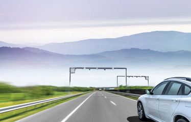 White car drives fast on the highway against the backdrop of a mountain range.