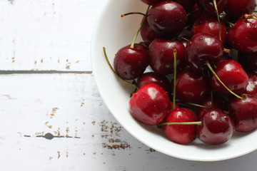 A handful of ripe cherries on a white plate in the right corner of the signature.