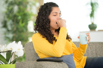 Fototapeta premium sleepy woman holding hot drink on knee on sofa