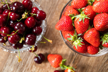 Fresh organic sweet cherries and strawberries in a glass bowls on wooden table