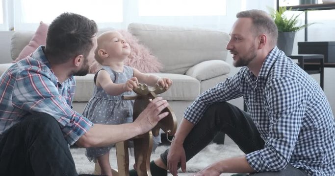 Two young men with cute baby girl having fun on rocking deer at home