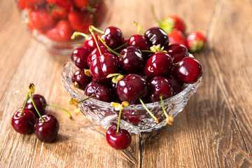 Fresh organic sweet cherries and strawberries in a glass bowls on wooden table