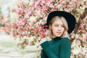 Close up portrait of young pretty caucasian curly blondie model posing outdoors in pink blossom garden. Beauty, nature concept