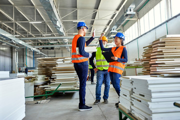 Happy colleagues in protective workwear high fiving in factory