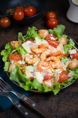 Caesar salad with shrimp on a dark wooden background.