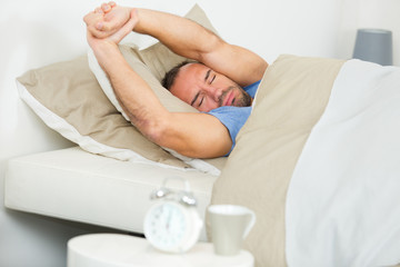 man in bed stretching arms over his head