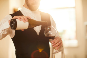 Mid section portrait of unrecognizable waiter pouring wine into glass at luxury restaurant lit by...