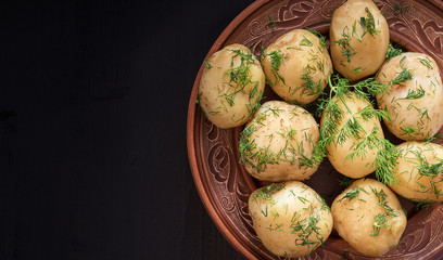Boiled potatoes with dill in a plate on a black wooden table.