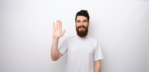 Young happy and cheerful bearded man making Hi, Hello gesture standing over white background in studio