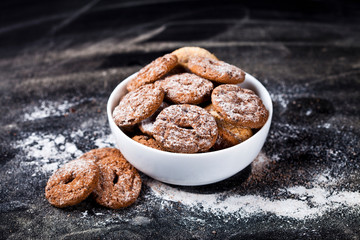Fresh baked chocolate chip and oat fresh cookies with sugar powder heap in white bowl on black background.
