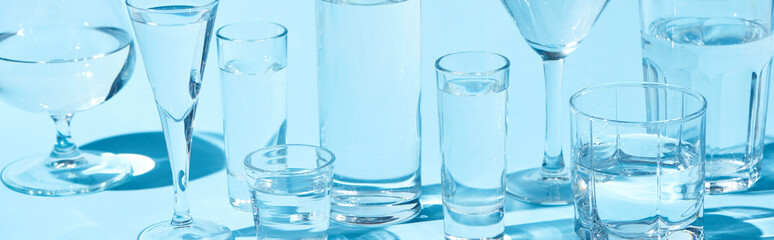 panoramic shot of transparent glasses with clear water on blue background
