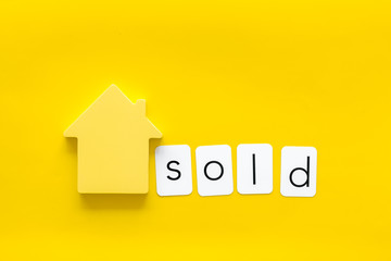 Mortgage credit concept with house toy and sold copy on yellow background top view