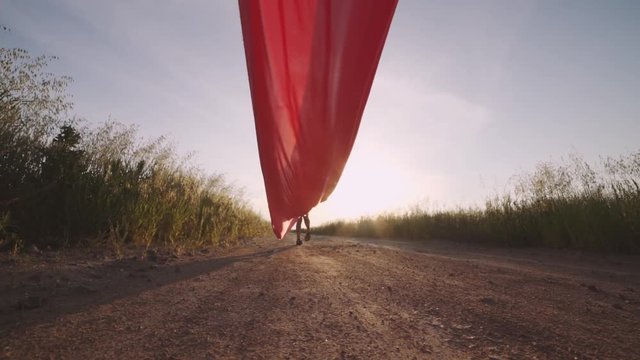 Woman with pieces of red cloth dance near the field with wind generators . Windmill on sunset. Slow motion. Stylish hipster woman
